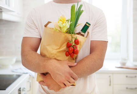 Man holding paper bag full of groceries on the kitchen background. Shopping and healthy food conceptの写真素材