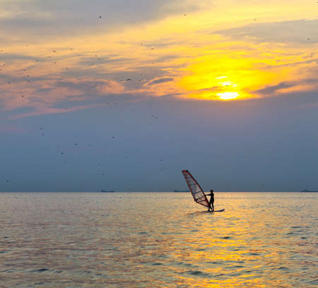 Windsurfer silhouette over sea sunset. Summertime fun, sport, activities, vacation and travel conceptの写真素材