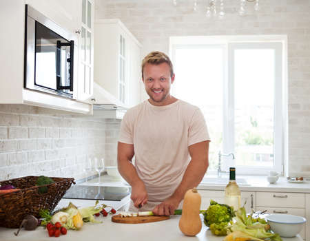 Handsome man cooking at home preparing salad in kitchenの写真素材