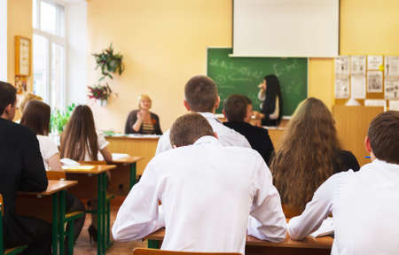 Rear view of students attentively listening to female student near the desk in the classroomの写真素材