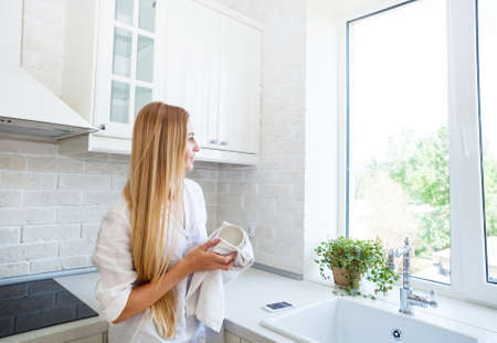 Happy woman doing the washing up in the kitchenの写真素材