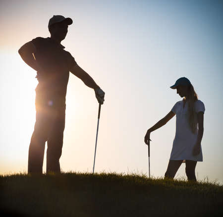 Male and female golfers playing golf at sunsetの写真素材