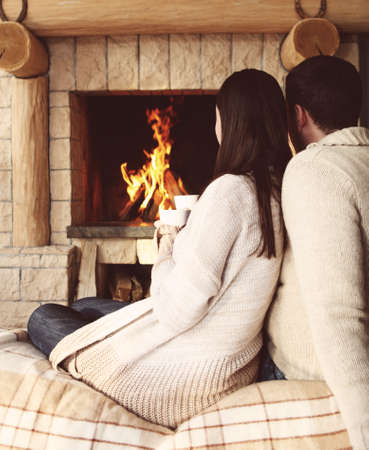 Couple holding cups with hot chocolate with marshmallows in front of lit fireplaceの写真素材