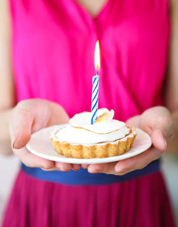 Lovely girl holding in hands cupcake with one candle. 