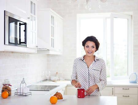 Happy woman preparing a cup of coffee in her kitchen wearing pajamas