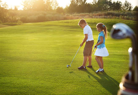 Casual kids at a golf field holding golf clubs. Sunsetの写真素材