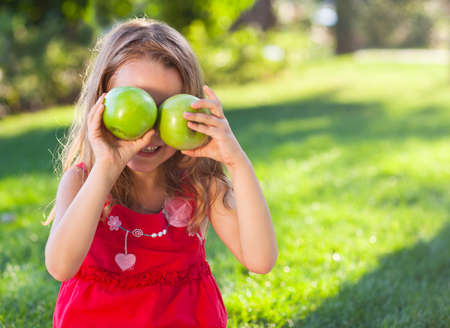 Funny litttle girl with green apples in the summer parkの写真素材