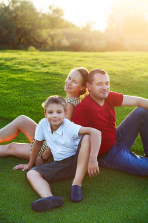 Happy family with son sitting on grass in the park. Summer sunsetの写真素材