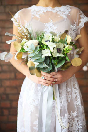 Unusual wedding bouquet with ranunculus, freesia, roses and white anemone in retro style at hands of a brideの写真素材