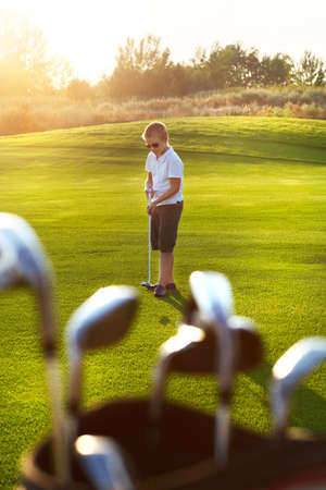 Casual kid at a golf field holding golf club. Sunsetの写真素材