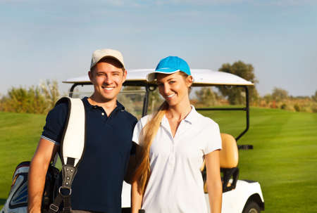 Young sportive couple playing golf on a golf course. Standing near the golfcar