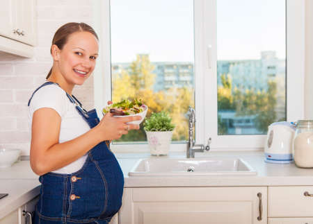 Happy pregnant woman with healthy food in kitchenの写真素材
