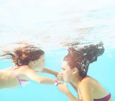 Happy smiling family underwater in swimming pool. Mother and child swim and having fun in water. Kids sport and fitness on family summer vacation. Active healthy holidayの写真素材