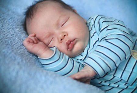 Peaceful baby lying on a bed while sleeping in a bright blue blanket
