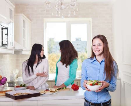 Cheerful teen girls preparing salad together in the kitchenの写真素材