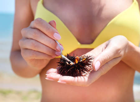 Woman holding a sea urchin with lemon for eating it on the beach