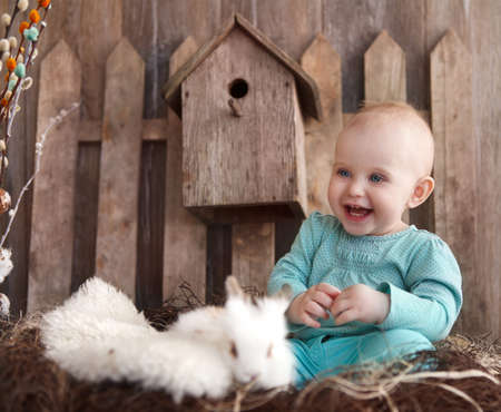 Portrait of an adorable baby girl and little white rabbit near the wooden background. Easter conceptの写真素材
