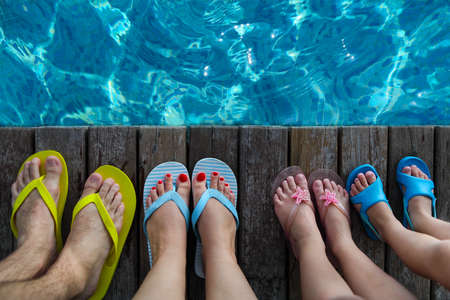Family wearing brightly colored flip-flops on wooden background near the pool. Summer travel and vacation conceptの写真素材