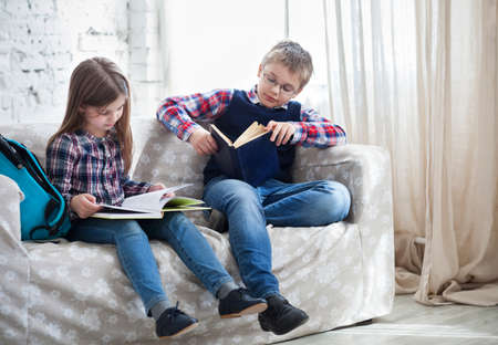 Children readind book in living room siting on the sofaの写真素材