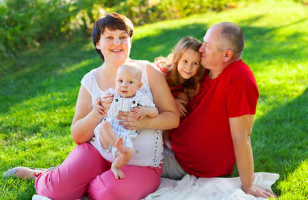 Happy family with two children sitting on green grass in the park