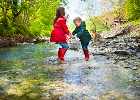 Happy children wearing rain boots jumping into a mountain riverの写真素材