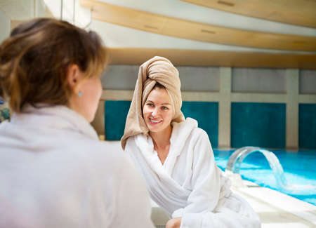 Two young women relaxing by the poolside wearing toweling robesの写真素材