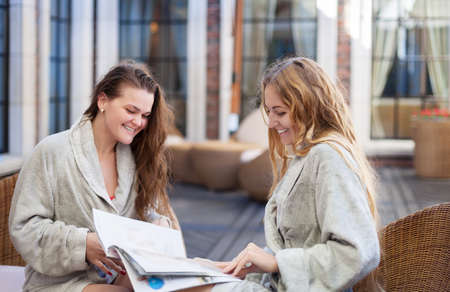 Two young women relaxing in the spa resort reading the magazine wearing toweling robesの写真素材