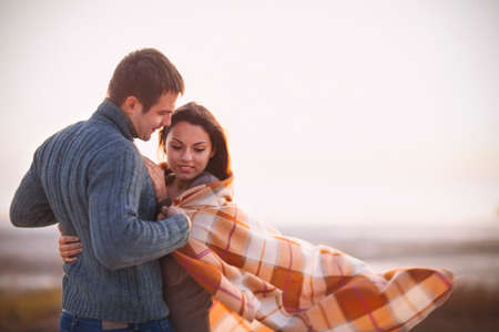 Closeup of young beautiful couple under blanket in a cold day near the sea after sunset. Noisy. Dusk timeの写真素材
