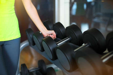 Fitness young woman with barbells on gym background