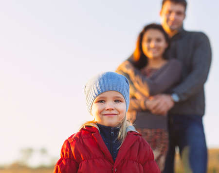 Portrait of the little girl with a funny hat outdoors and man and woman holding hands of smiling at...
