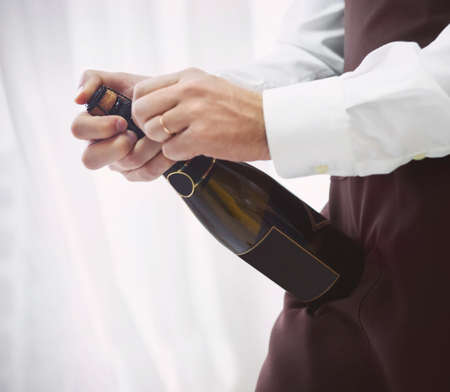 Professional male waiter in uniform opening bottle of champagne. DOF. Natural light. Photo in motionの写真素材