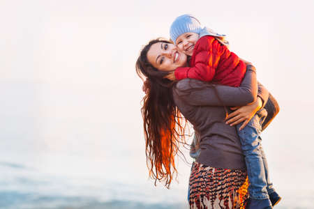 Mother and baby at the beach. Happy mum and baby girl walking at beach in autumnの写真素材