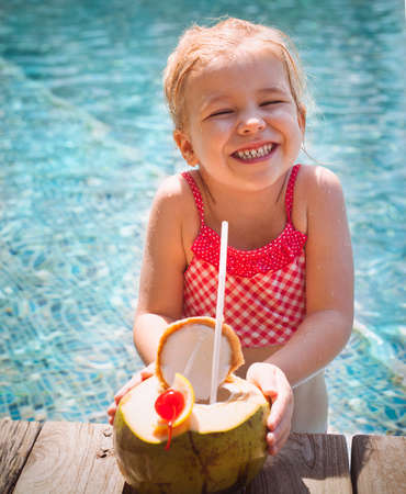 Cute funny little girl drinking coconut at the pool. Summer vacation conceptの写真素材