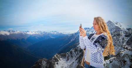Blond woman photographing winter landscape mountains and snow with cell phoneの写真素材