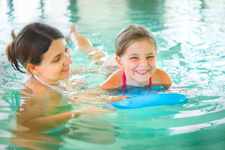 Mother learning to swim her little daughter in an indoor swimming pool. Having fun together. Kids swimming concept.の写真素材