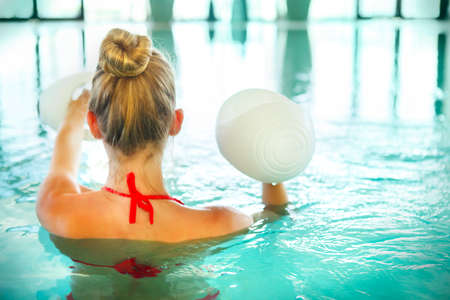 Blond young woman doing aqua aerobics with foam dumbbells in swimming pool at the leisure centreの写真素材