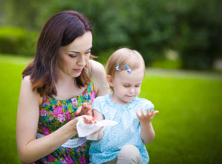 Mother using wet wipes for her daughter on white park backgroundの写真素材