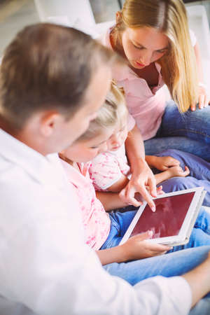 Attractive happy family of mother, father and daughters sitting on a sofa at home having fun using a tablet computer. DOF. Close upの写真素材