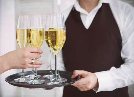 Professional male waiter in uniform serving champagne. Woman taking one glass of champagne. DOF. Natural light. Photo in motionの写真素材