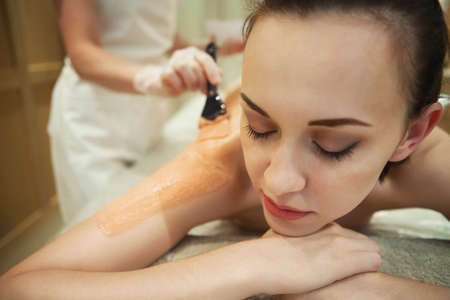 Beautiful relaxed woman having clay body mask apply by beautician in the spa salonの写真素材