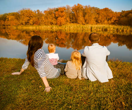 Happy family - mother, father and daughters relaxing at autumn countryside with lake