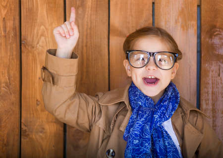 Funny little girl with glasses on wooden wall background