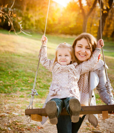 Happy mother and her little baby swing on the background of trees and sky in the autumn parkの写真素材