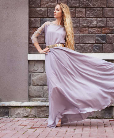 Beautiful blond woman in long dress walking outdoorsの写真素材
