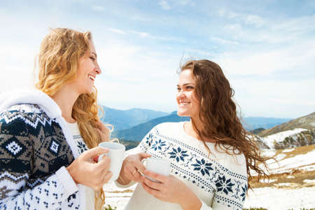 Two happy female friends enjoying hot drink In cafe at ski resort