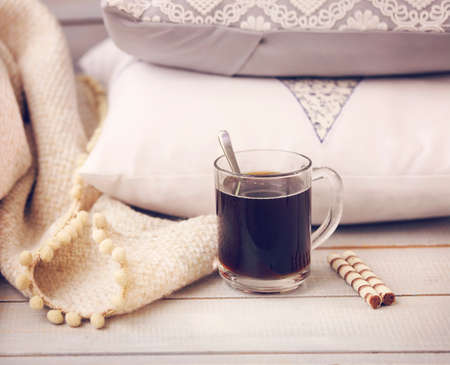 Cozy still life with coffee, pillows and plaid on the light wooden background. Close up