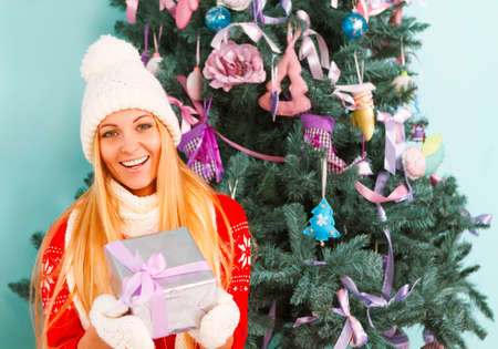 Happy young woman with Christmas present in her hands by the Christmas treeの写真素材