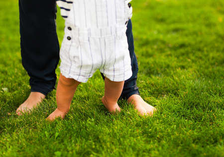 Baby boy taking first steps and mother helping in summer gardenの写真素材