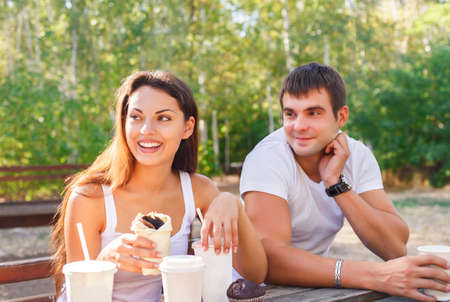 Man and woman or young couple drinking coffee and sitting in city park in summer