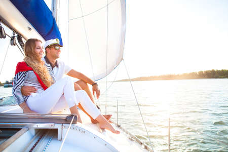 Young smiling couple on a sailing boat at summer sunsetの写真素材